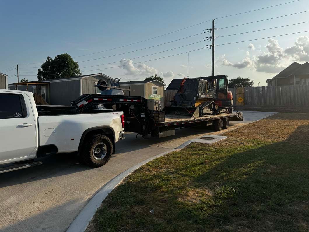 A white truck is towing a tractor down a street.