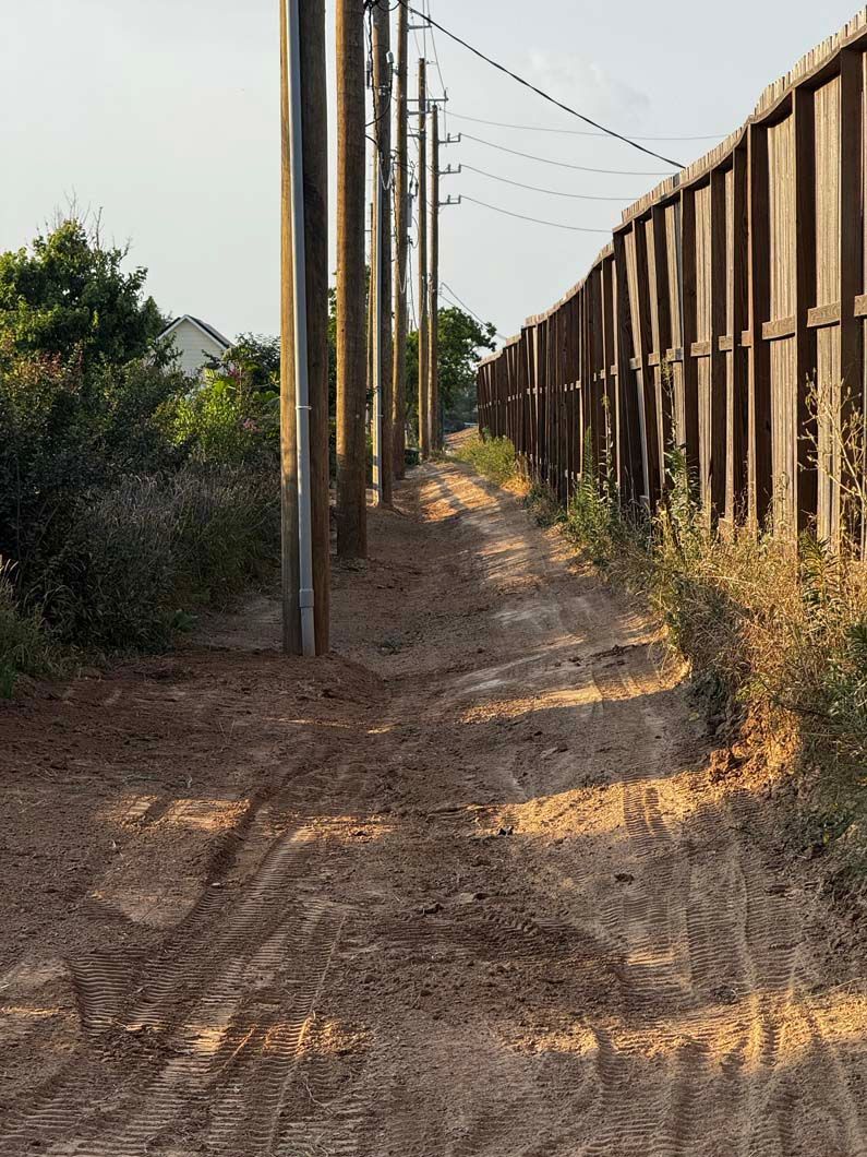 A dirt path leading to a wooden fence surrounded by power lines.