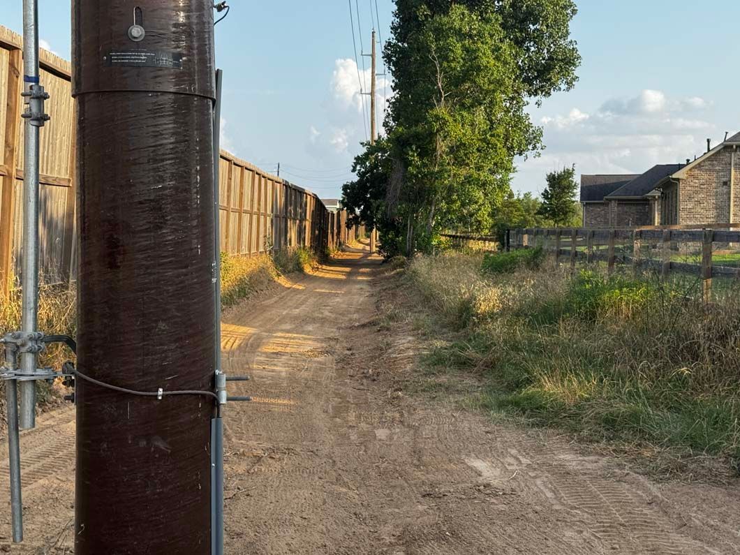A dirt road with a fence and a pole in the middle of it.
