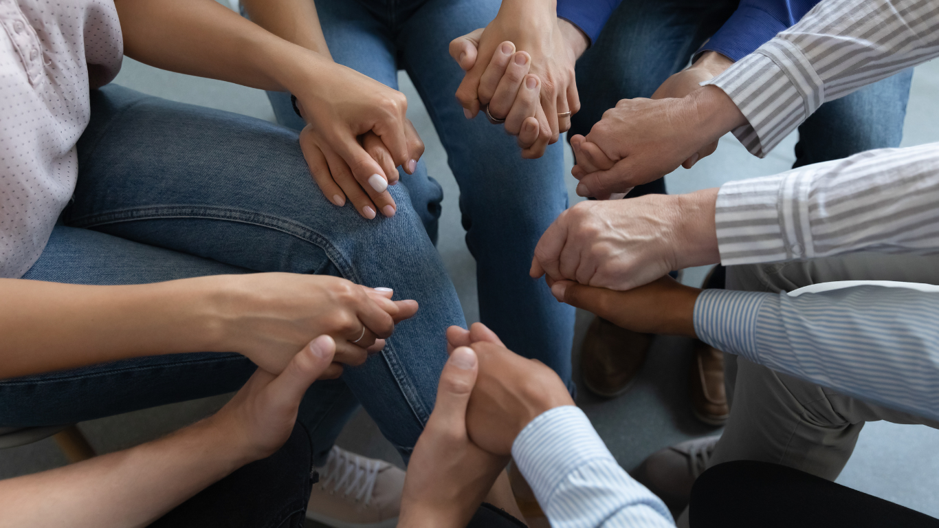 A group of people are sitting in a circle holding hands.