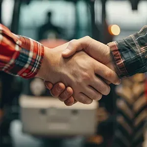 Handshake between two people in plaid shirts in a farm setting