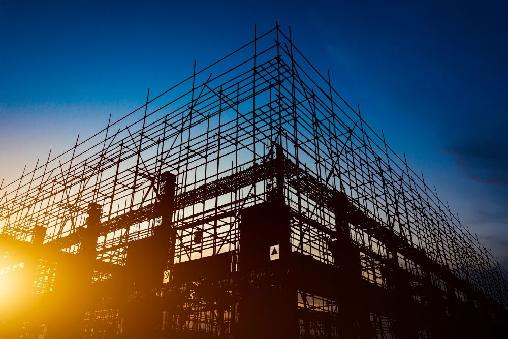 Silhouetted construction scaffold at sunset with a worker against a blue-orange sky