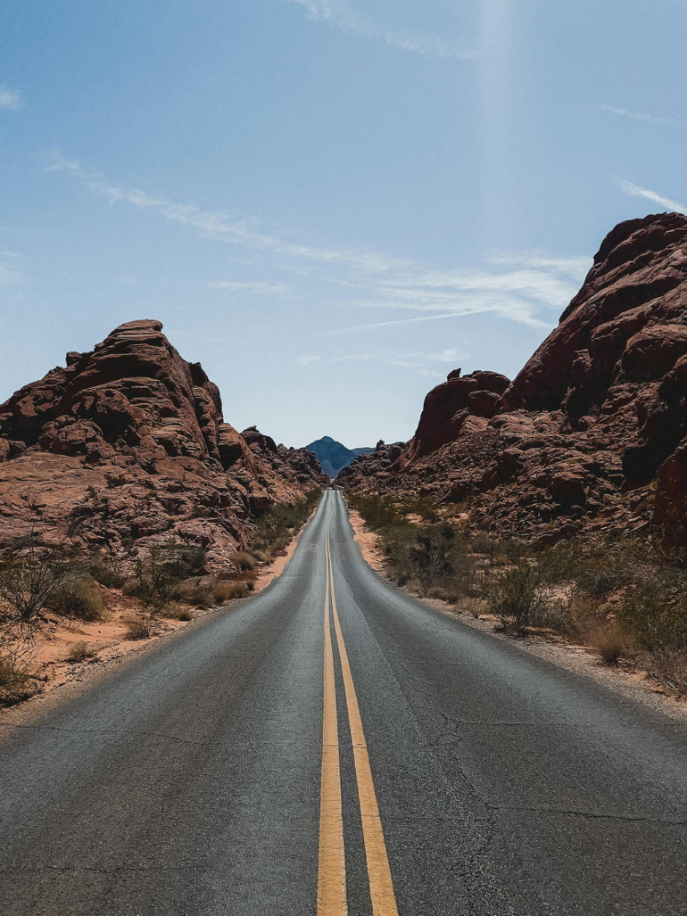 Straight desert road leading between rocky canyon walls under a clear blue sky