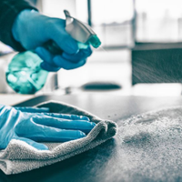 Blue-gloved hands cleaning a countertop with spray and cloth in a kitchen or lab setting