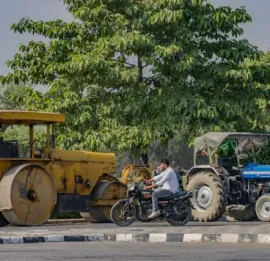 Road roller, motorcycle, and tractor stopped on a roadside under a large tree