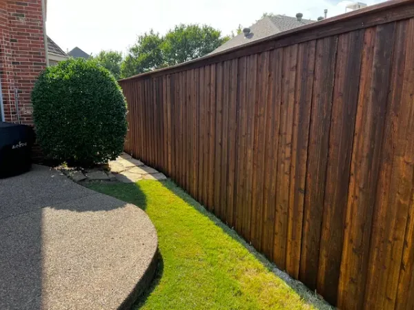 A wooden fence surrounds a lush green lawn in a backyard.
