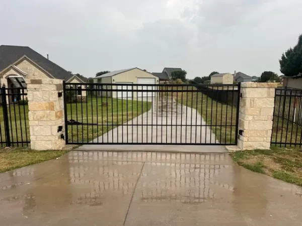 A black metal gate is open to a driveway leading to a house.