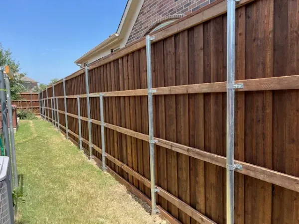 A wooden fence with metal posts is sitting next to a brick house.