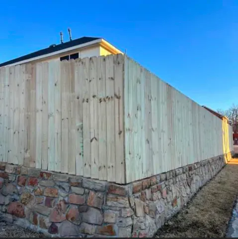 A wooden fence surrounds a stone wall next to a house.