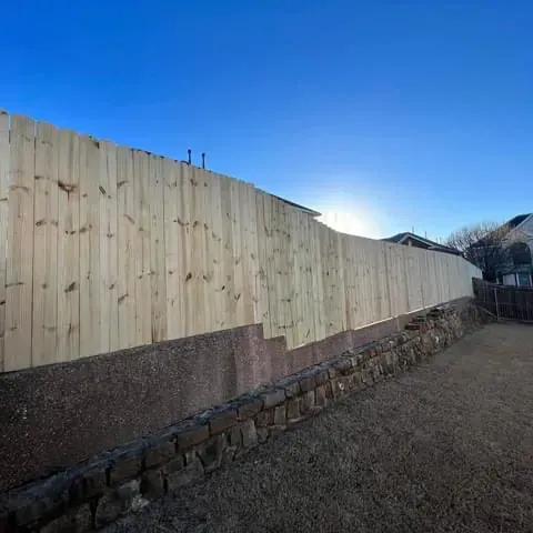 A wooden fence surrounds a stone wall in a backyard.