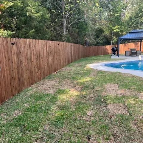 A wooden fence surrounds a swimming pool in a backyard.