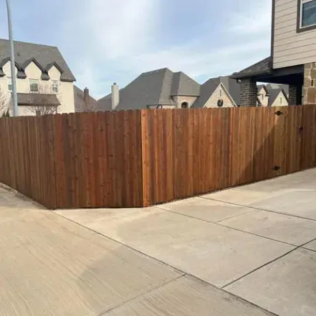 A wooden fence is surrounding a driveway in front of a house.