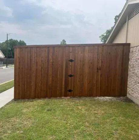A wooden fence is sitting in the grass next to a brick building.