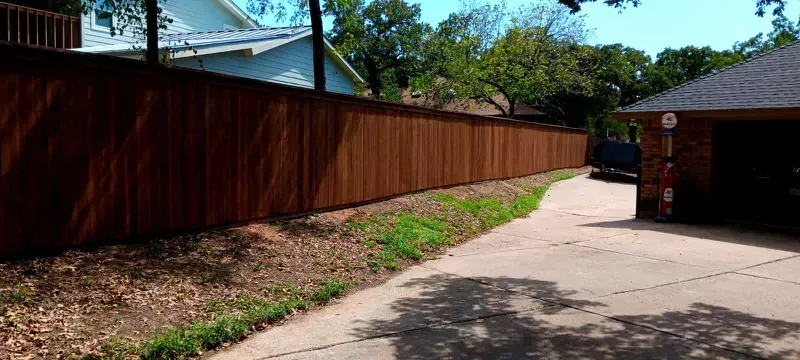 A wooden fence surrounds a driveway leading to a house.