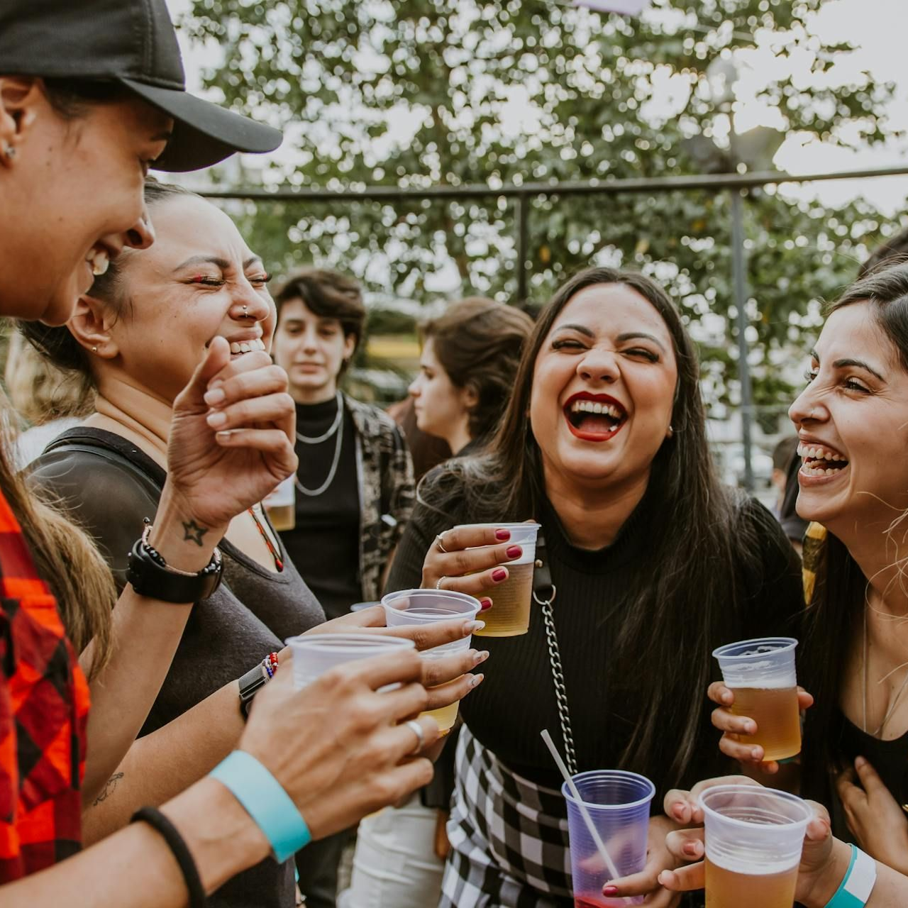 Group of people laughing, holding drinks outdoors.