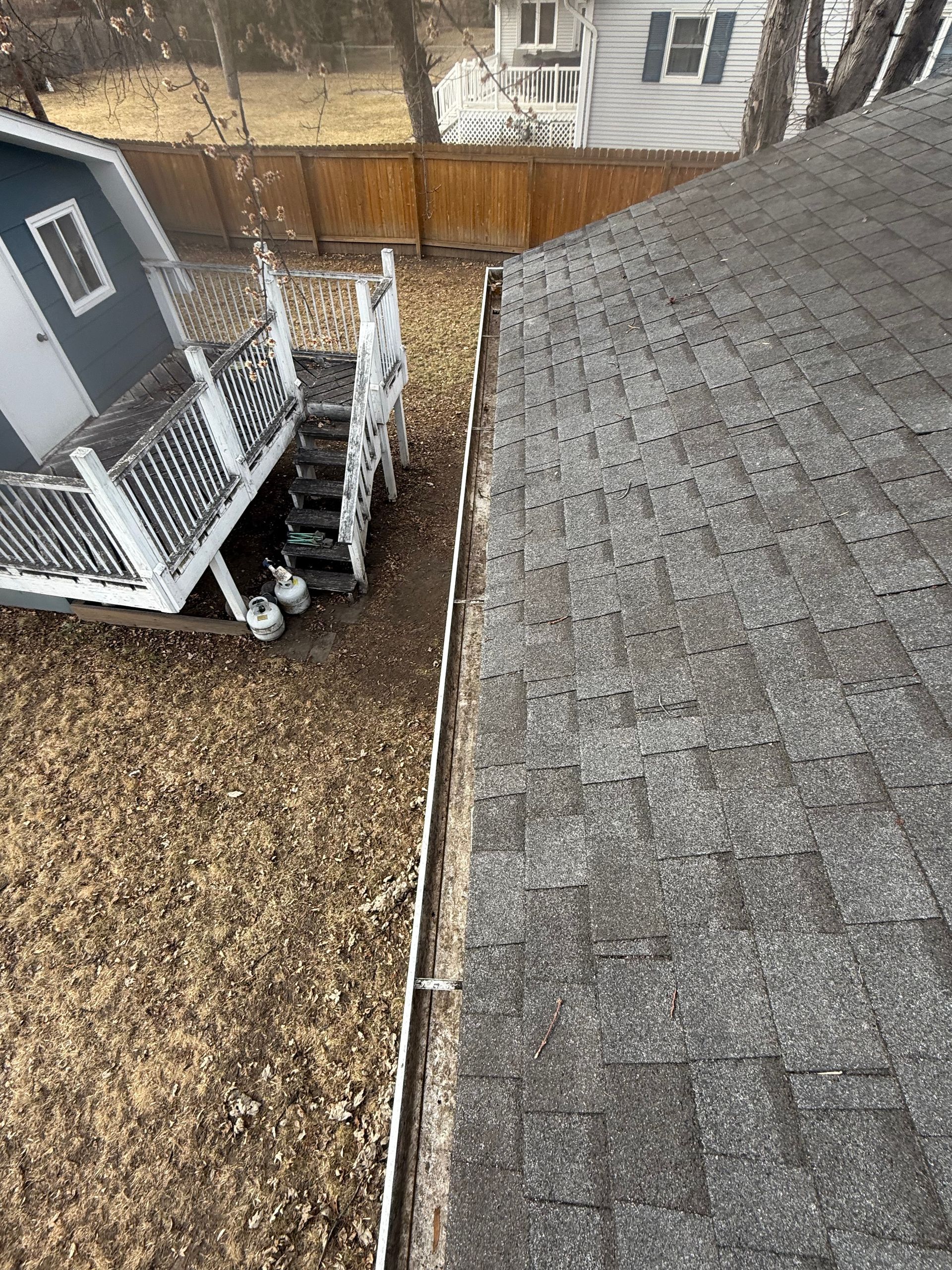 Overhead view of a house roof, lawn, shed, and fence. Brown lawn, gray roof, white trim.