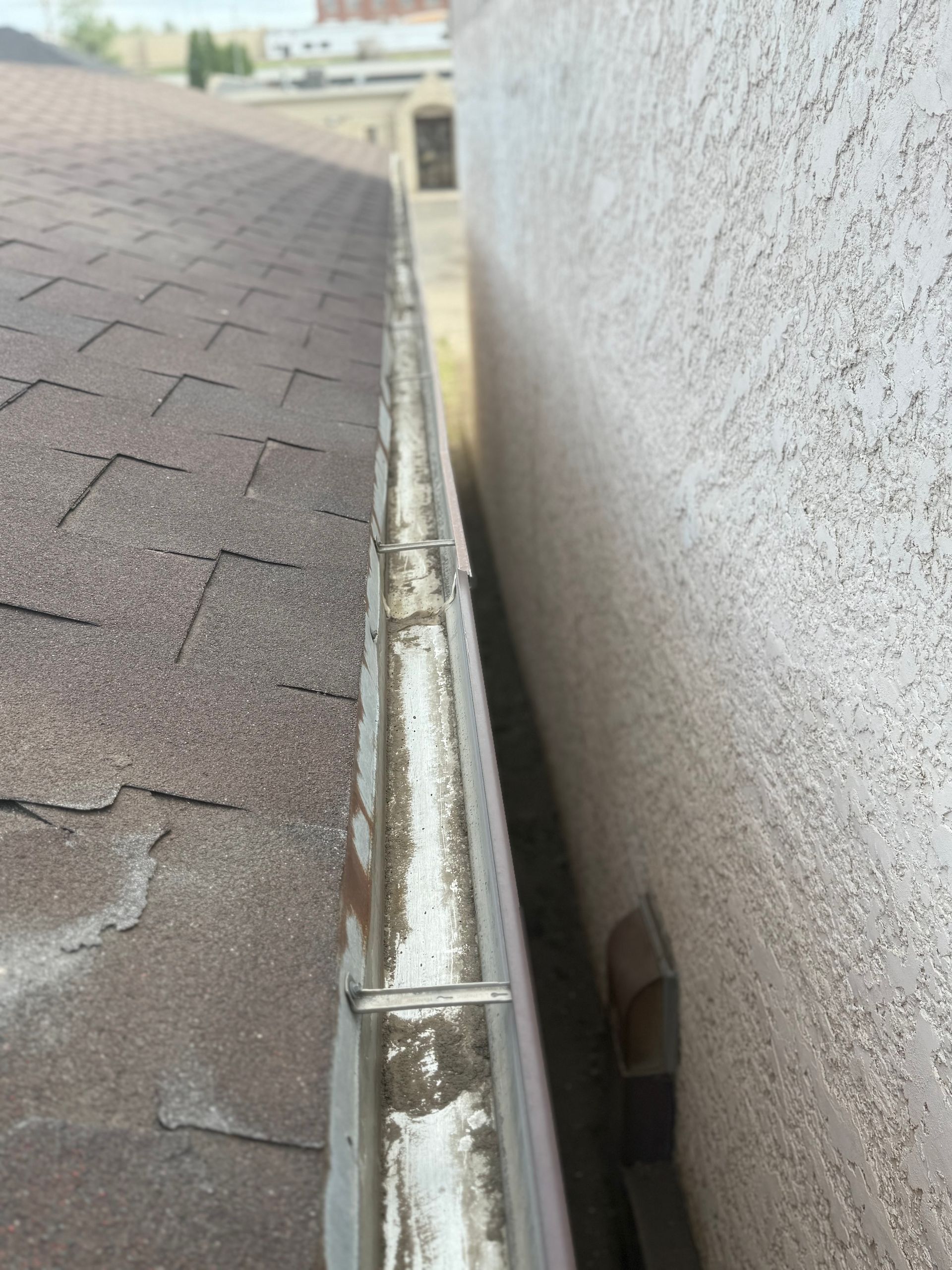 Gutter along a roof edge next to a stucco wall, showing debris buildup.