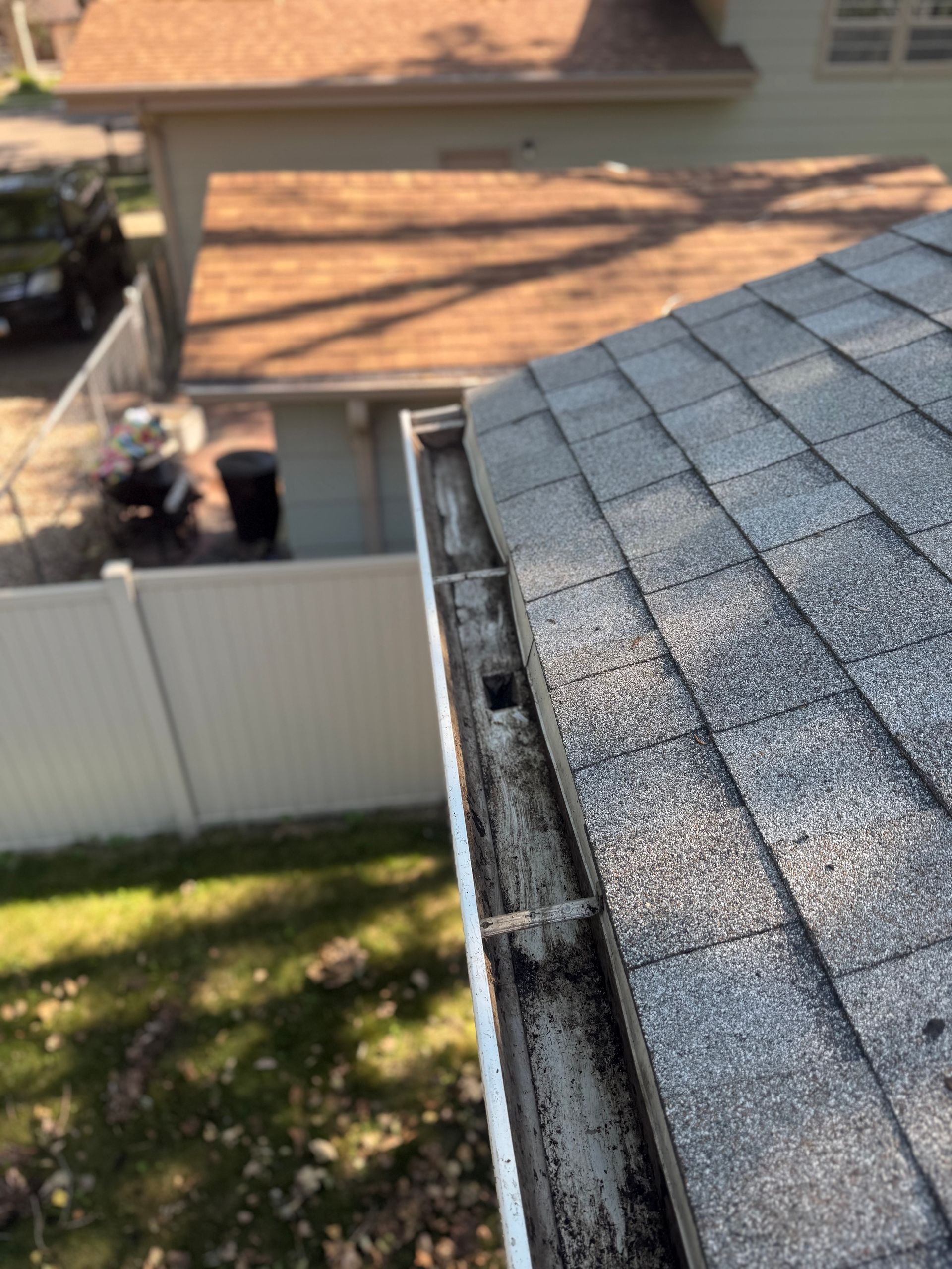 Roof with a dirty gutter, viewed from above, with a fence and yard in the background.