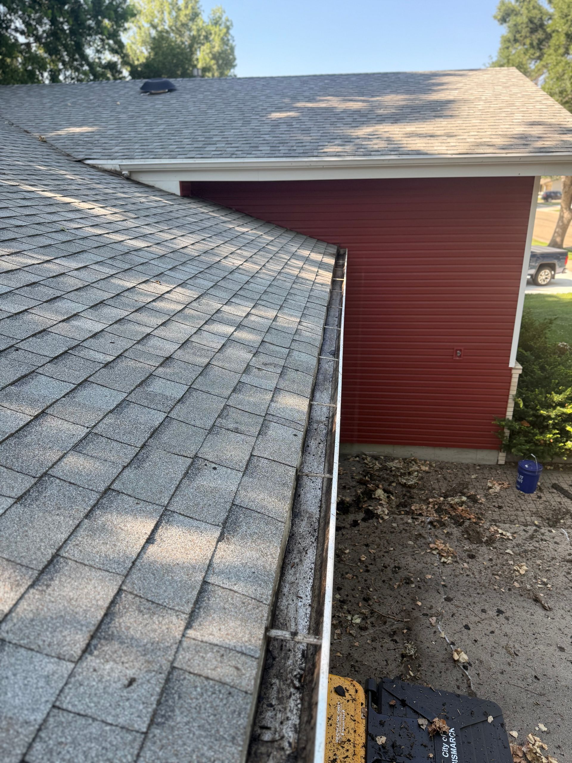 Roof of a house with a red-sided garage attached. The roof has algae and debris in the gutter.