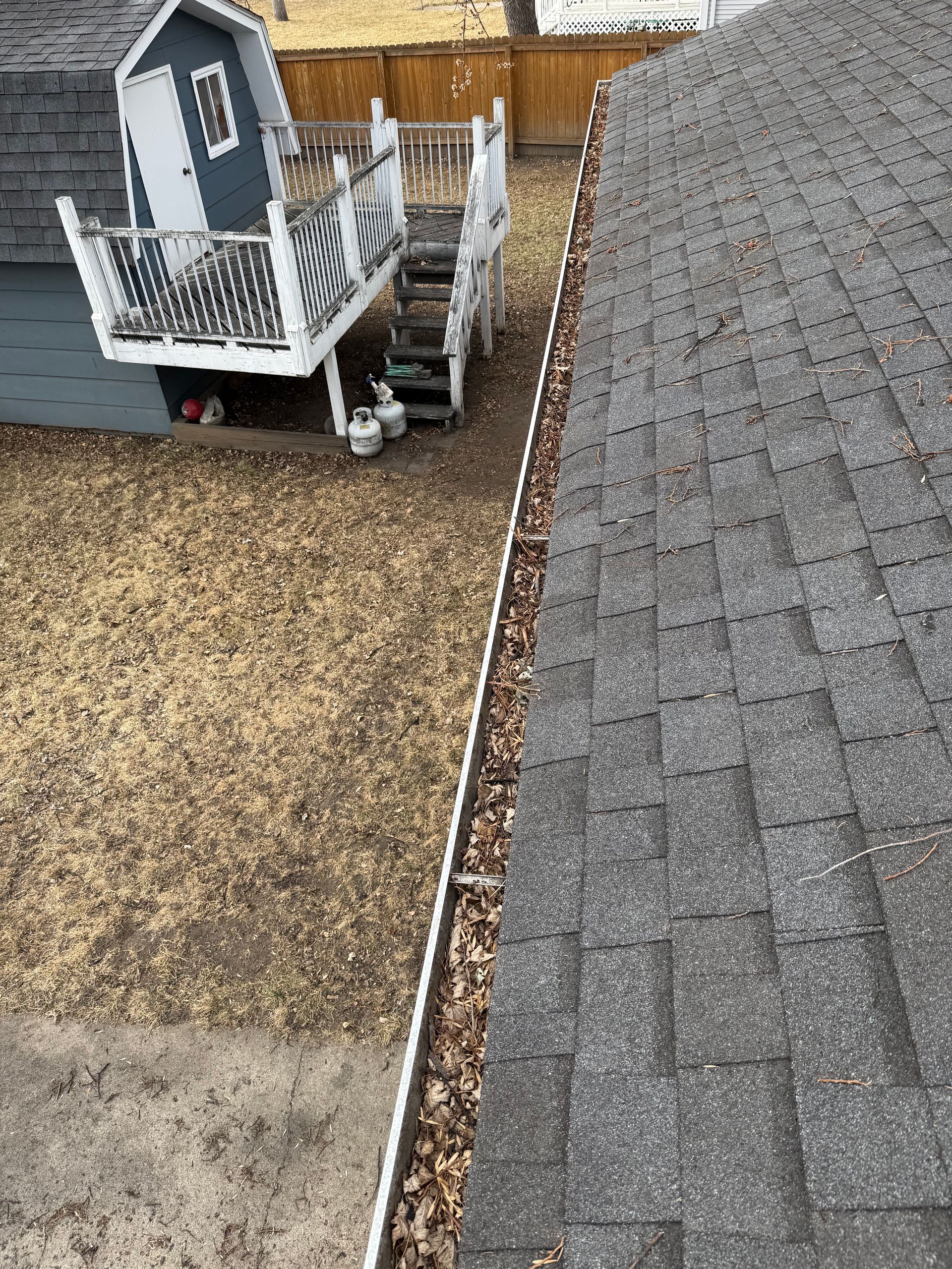 Gutter filled with leaves alongside a gray-shingled roof. A playset and yard are visible in the background.