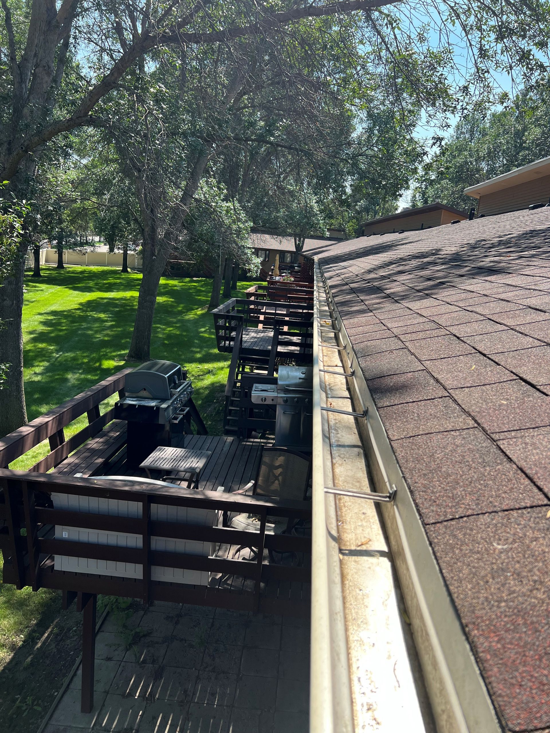 View from a rooftop, looking at a deck, trees, and lawn on a sunny day.