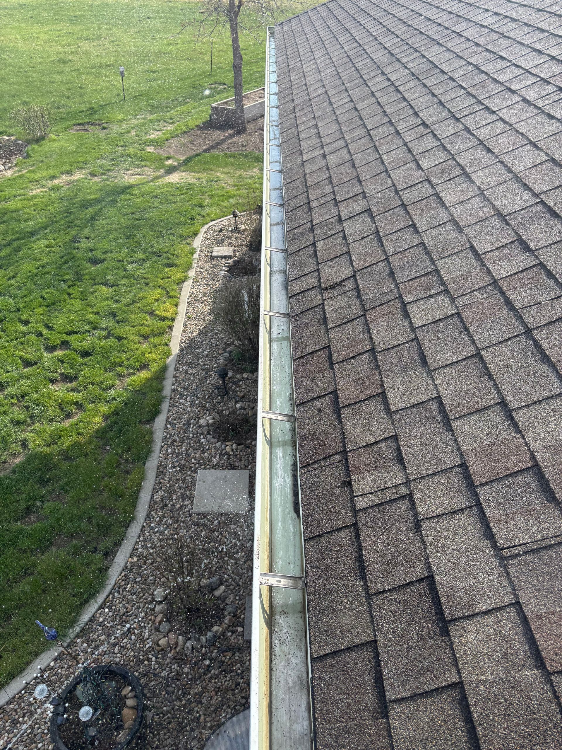 Gutter along roof edge with brown shingles, green grass, and gravel landscaping.