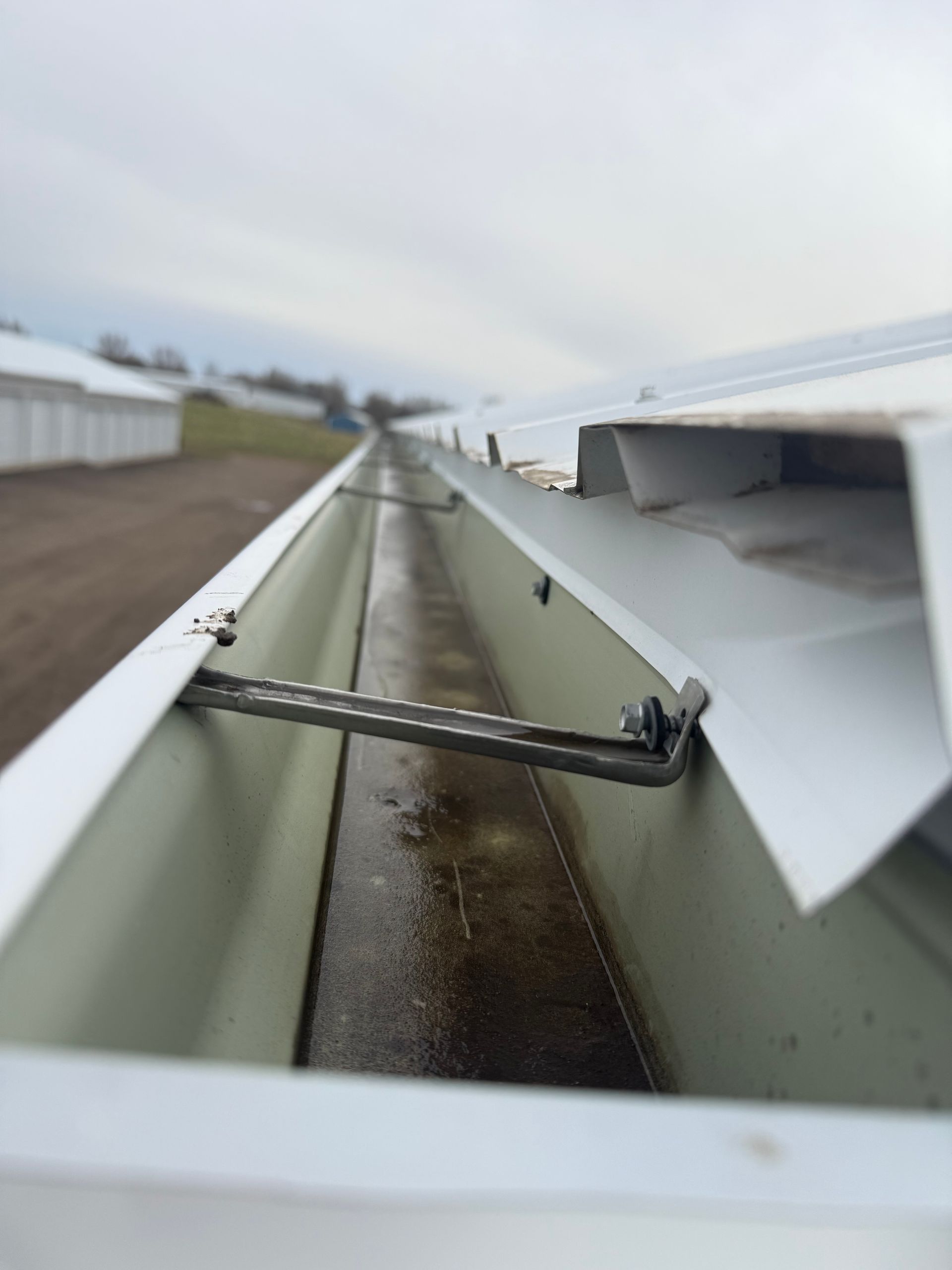 View inside a white gutter with a horizontal bar, looking towards a distant building on a cloudy day.