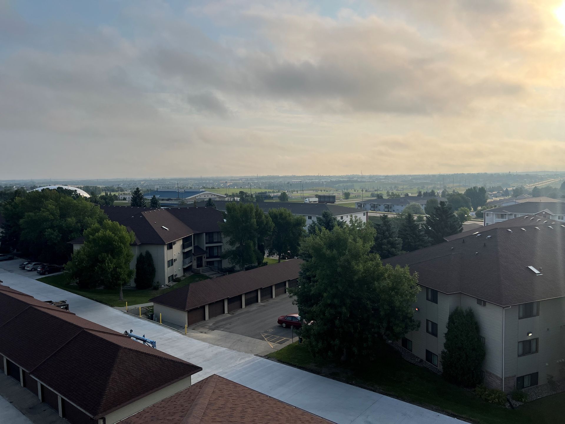 Overhead view of apartments and garages under a cloudy sky with hints of a distant field.