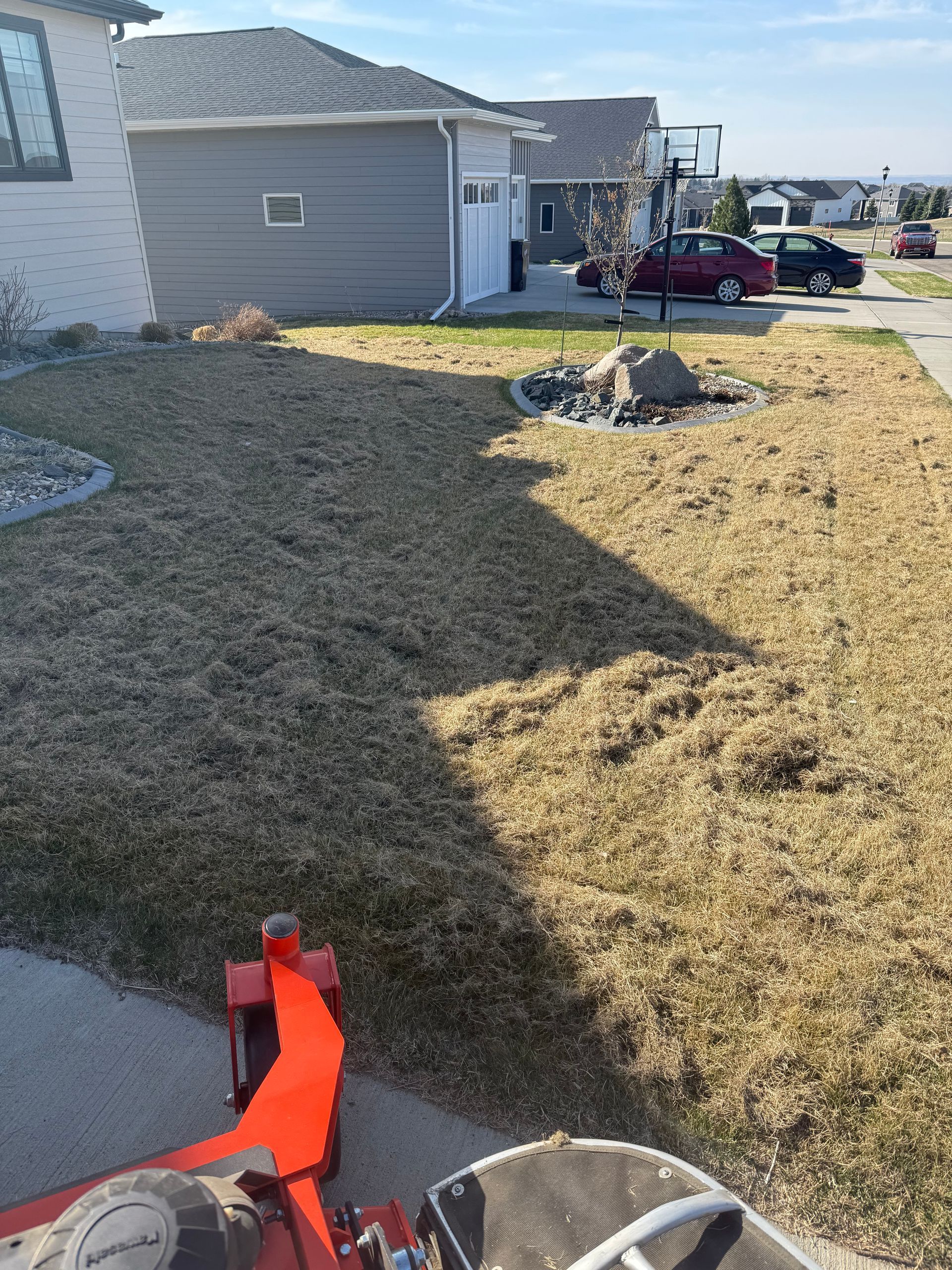Lawn being mowed with a red zero-turn mower on a sunny day. The grass is dry and brown.