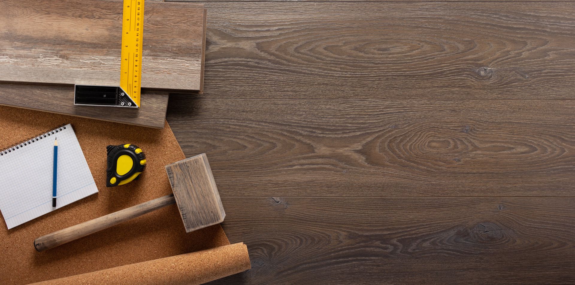 Ein Holzboden mit einem Maßband, einem Hammer, einem Lineal und einem Notizbuch darauf.