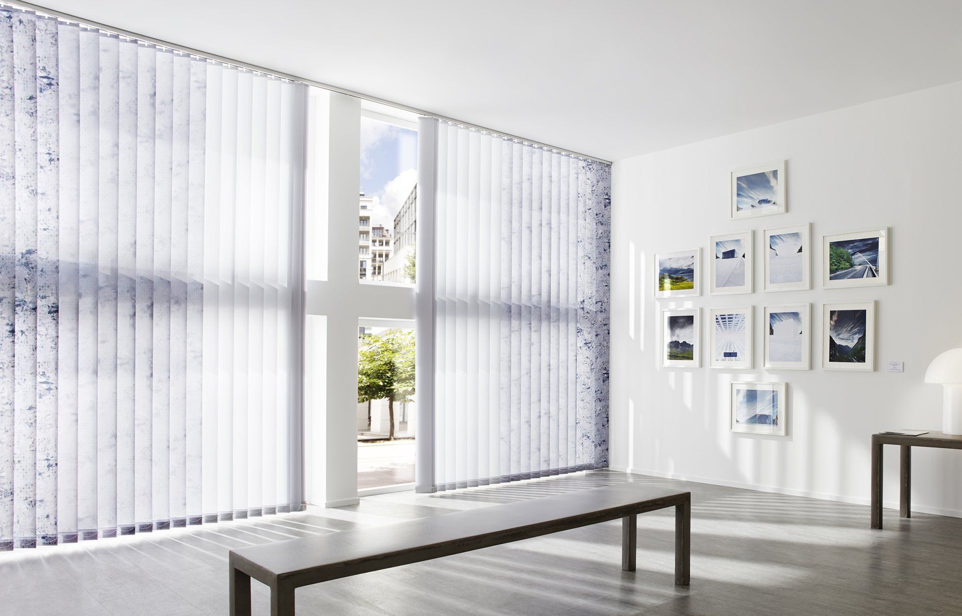 Weißer Raum mit Tisch und Bildern an der Wand und weißen Lamellenvorhängen