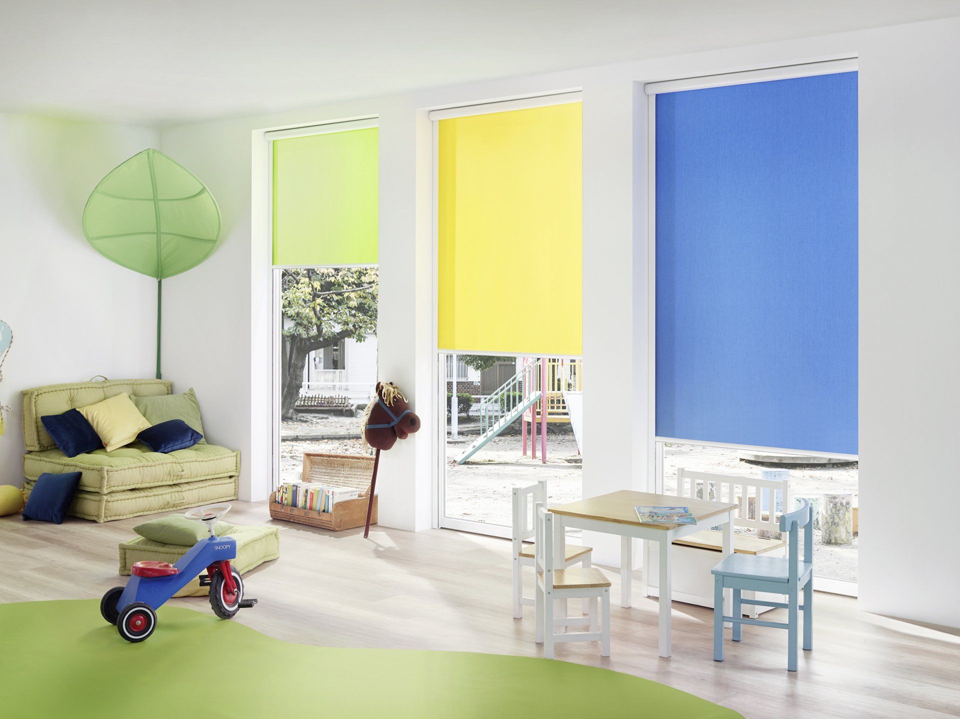 Kinderzimmer mit grünem Teppich und Miniaturtisch und bunten Fensterrollos in blau, gelb und grün