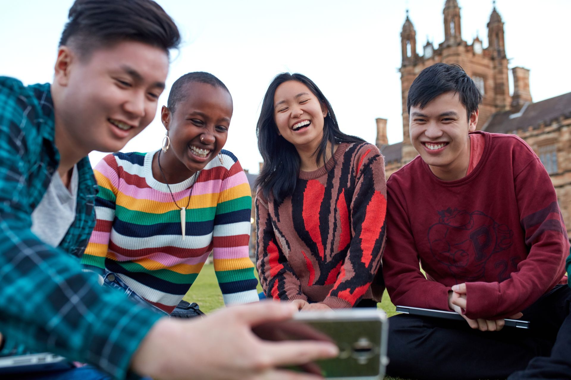 Four friends smiling outdoors, gathered around a phone with a historic building in the background