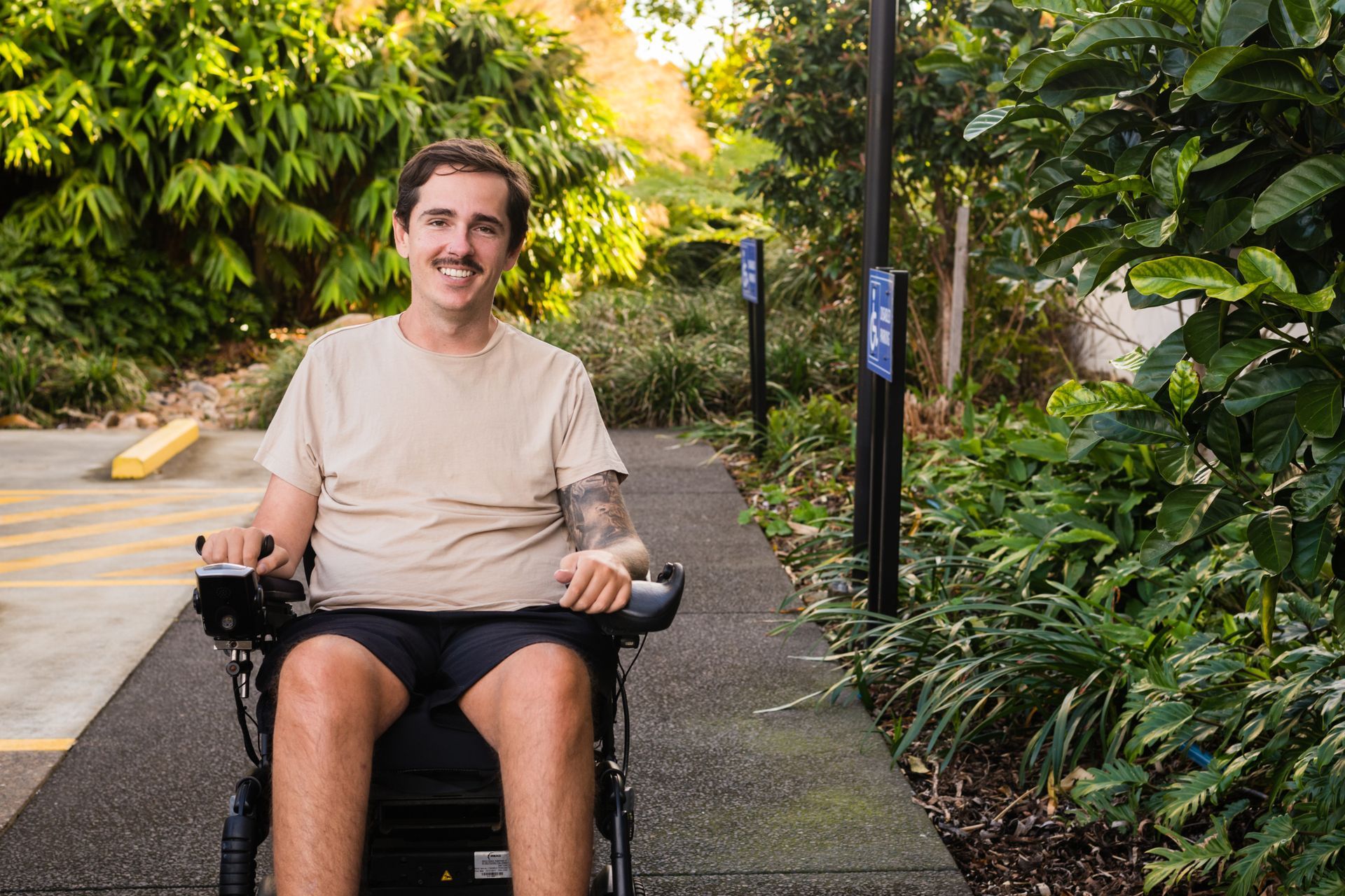 Person in a wheelchair smiling on a garden path surrounded by lush greenery