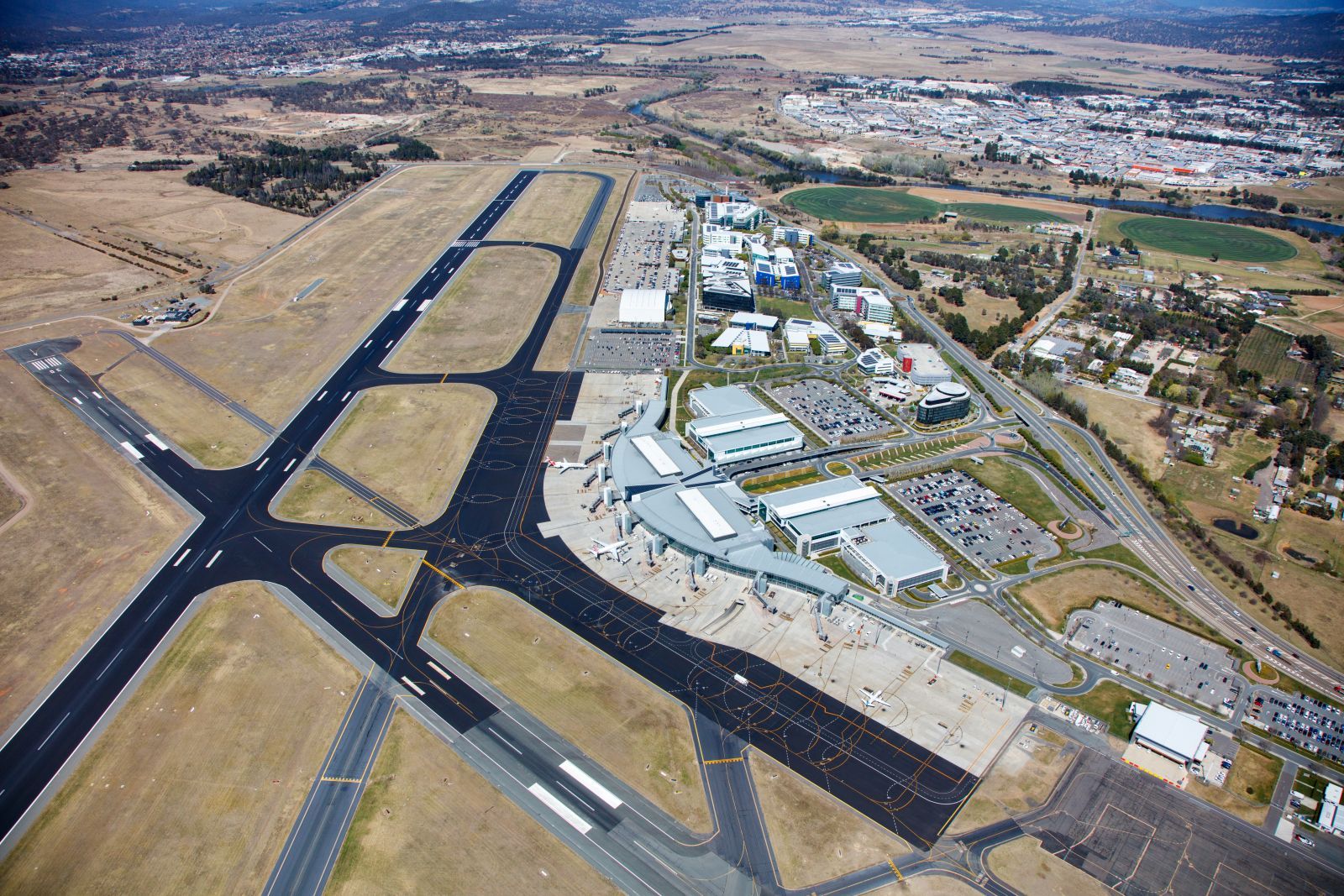 Aerial view of an airport runway and taxiways beside terminal buildings and surrounding town.
