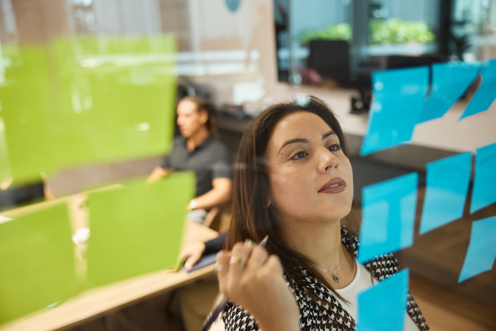 Woman writing on a glass wall covered with colorful sticky notes in an office meeting room