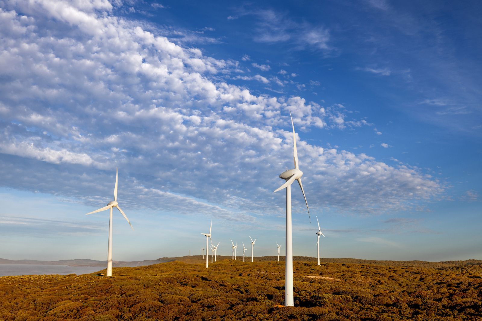 Wind turbines on a grassy hillside under a blue sky with scattered clouds.