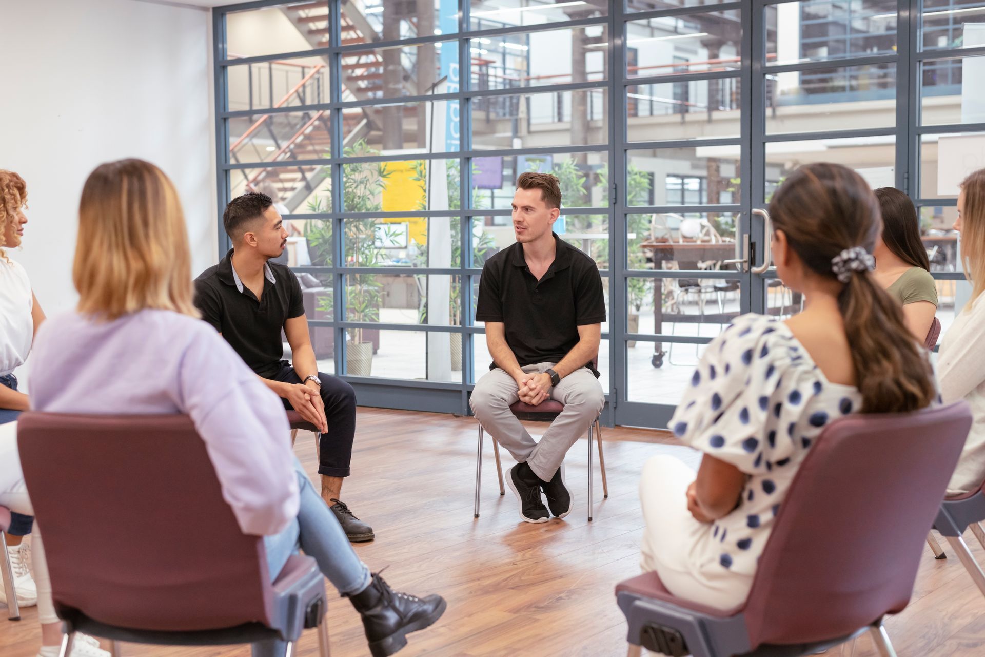 Small group seated in a bright meeting room, discussing around a circle of chairs.