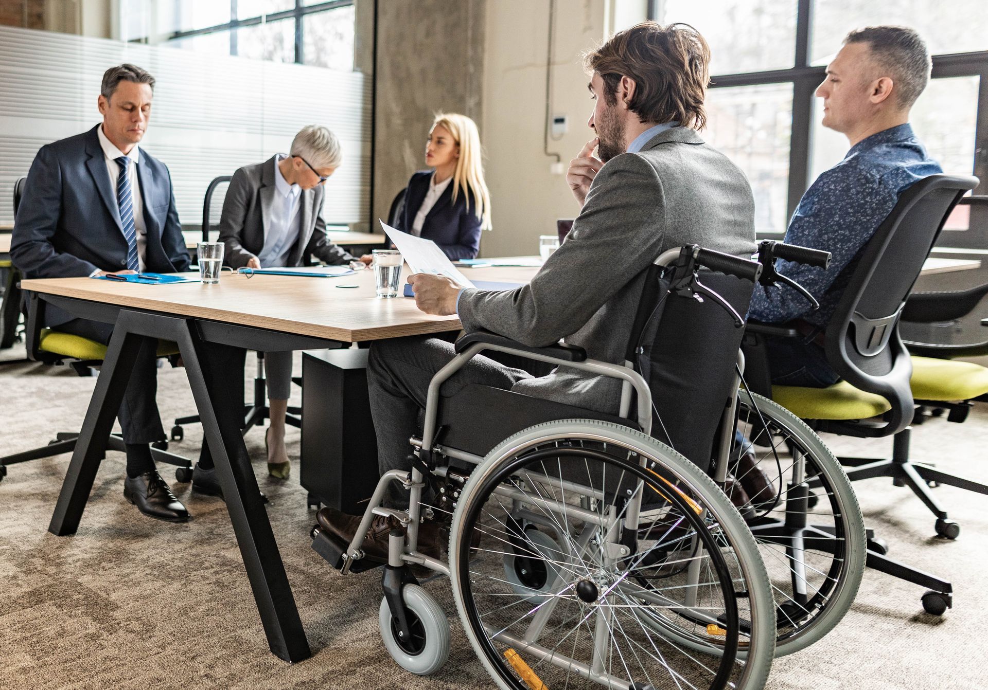 Business meeting with four people, including a wheelchair user, seated around a table in a bright office