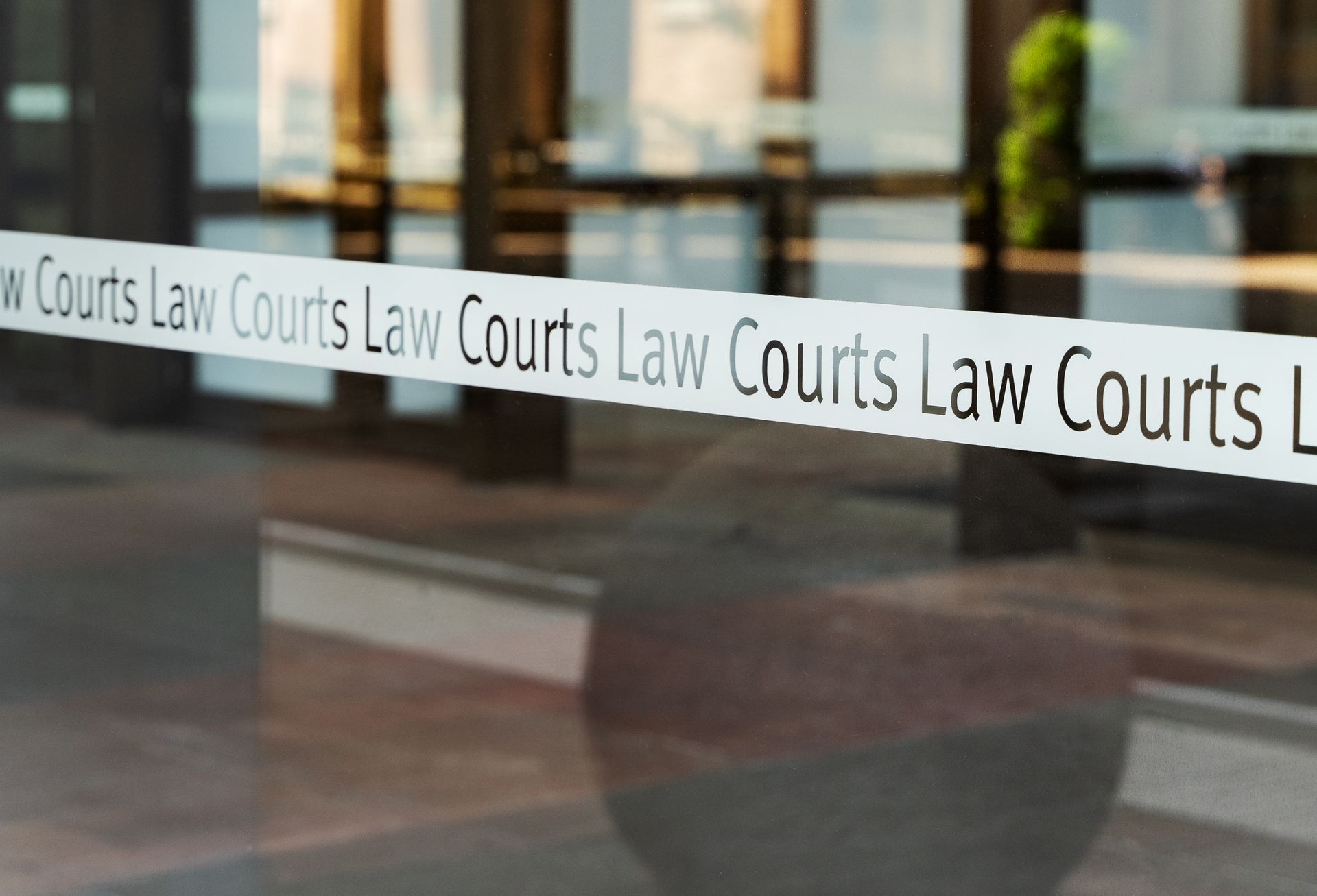 Glass law office door with repeated “Law Courts” frosted lettering reflected on the surface