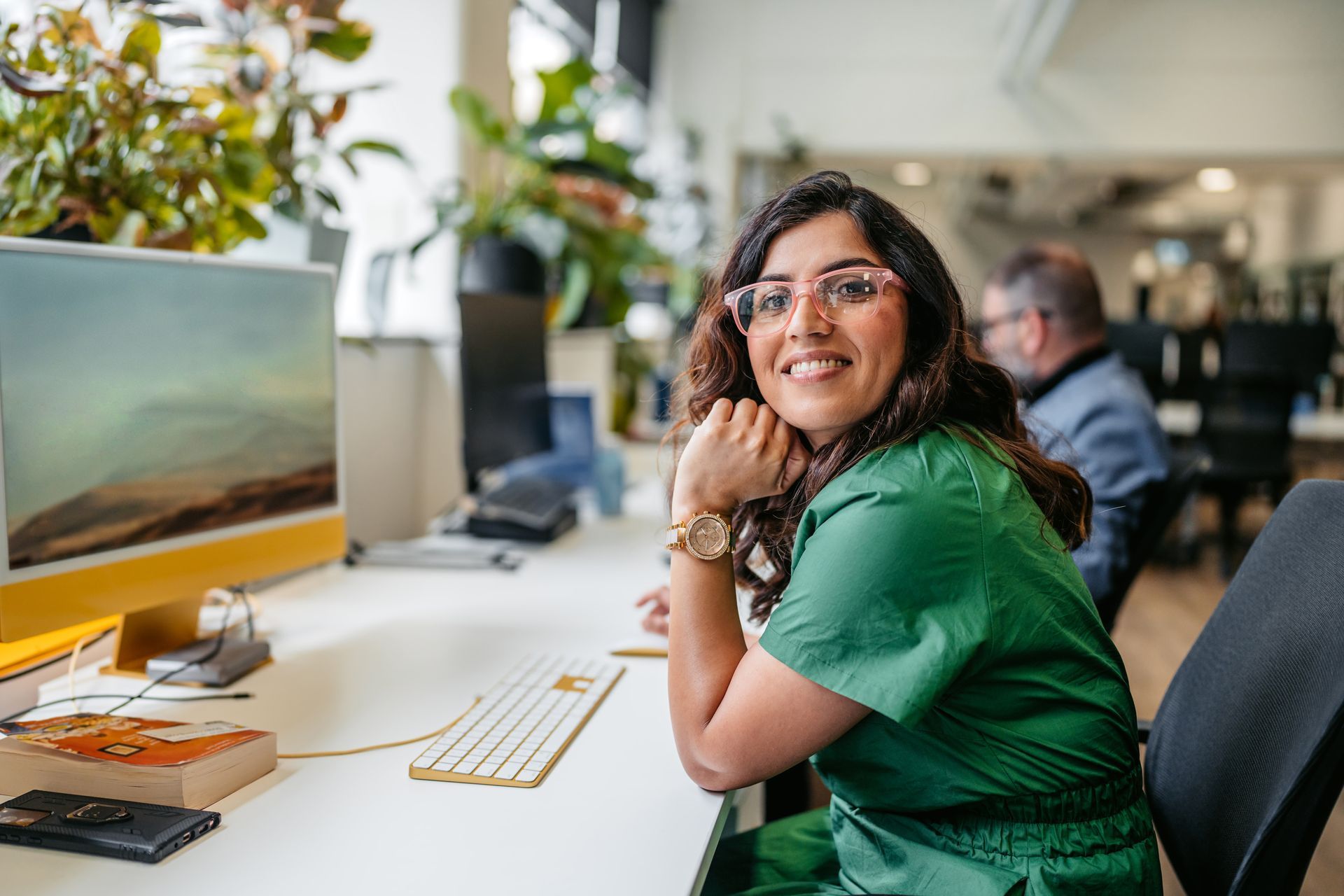 Woman in green dress smiling at a desk with a computer in a bright office