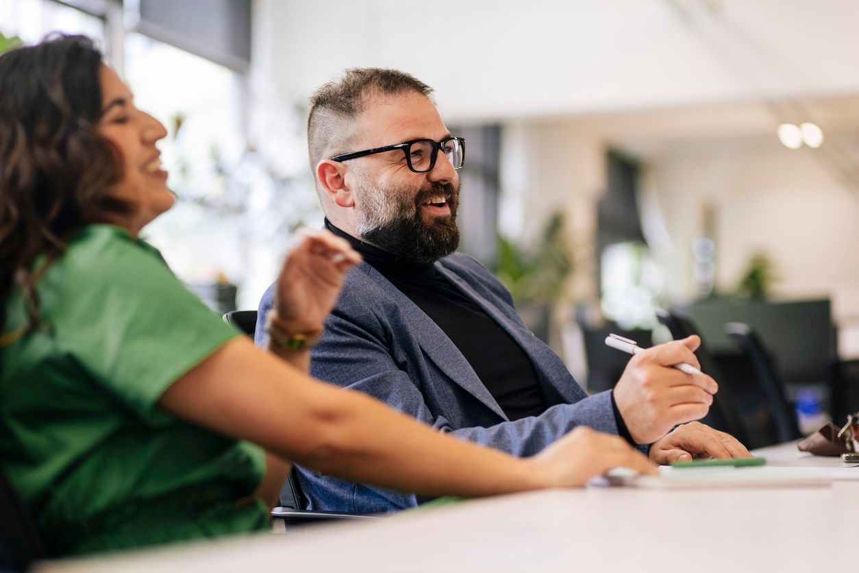 Two coworkers smiling and talking at a desk in a bright office