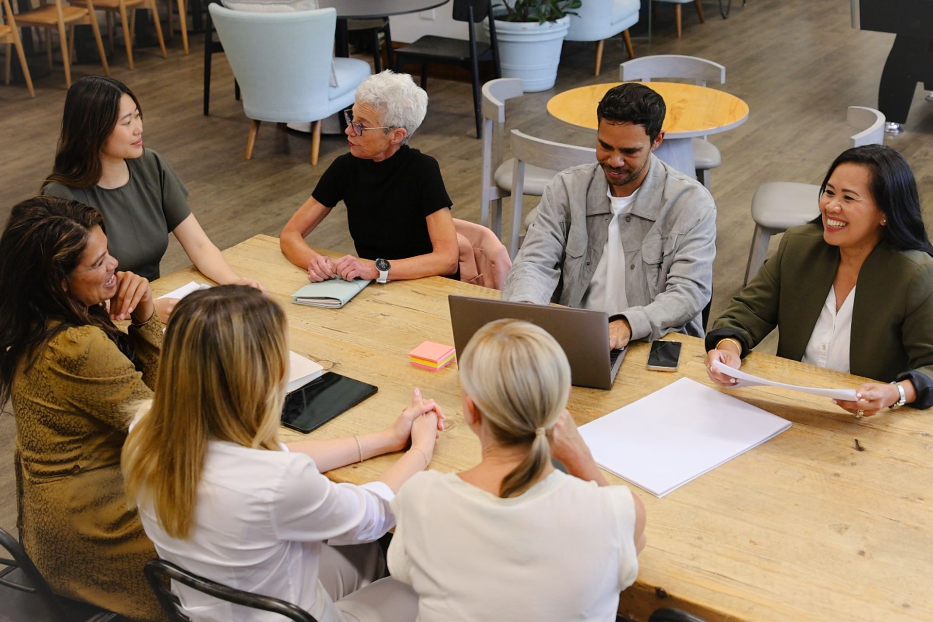 People seated around a table in a meeting, discussing papers in a bright office lounge.