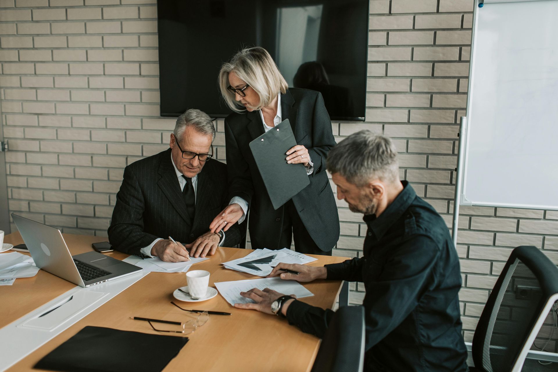 Three coworkers review documents at a conference table in a modern office meeting room.