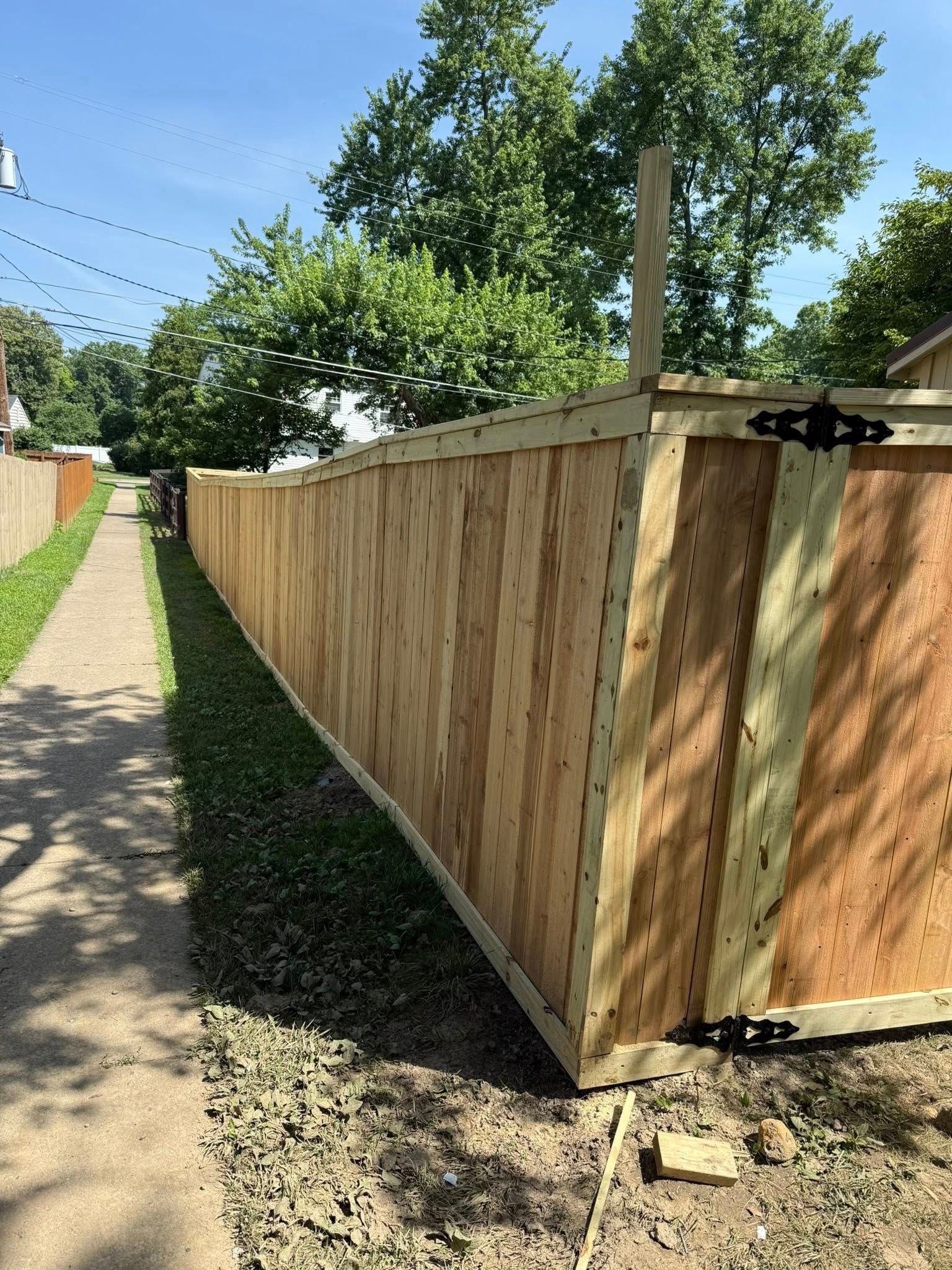 Wooden fence along a sidewalk with green grass and trees on a sunny day.