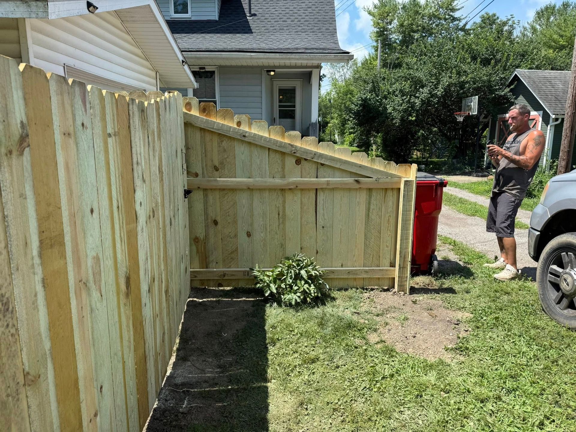 Man next to new wooden fence and red trash can in a yard.