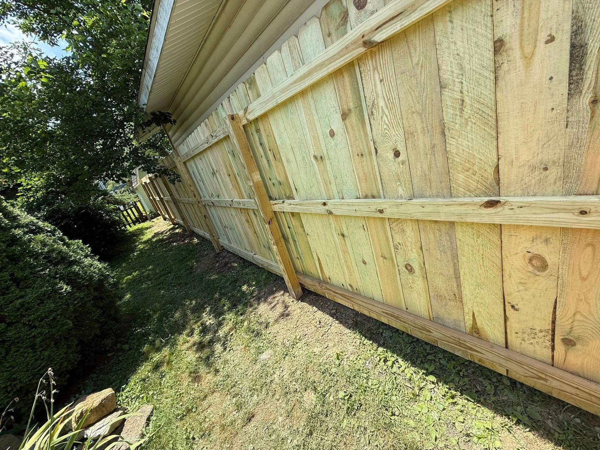 Wooden fence next to a building with white siding, green grass and bushes.