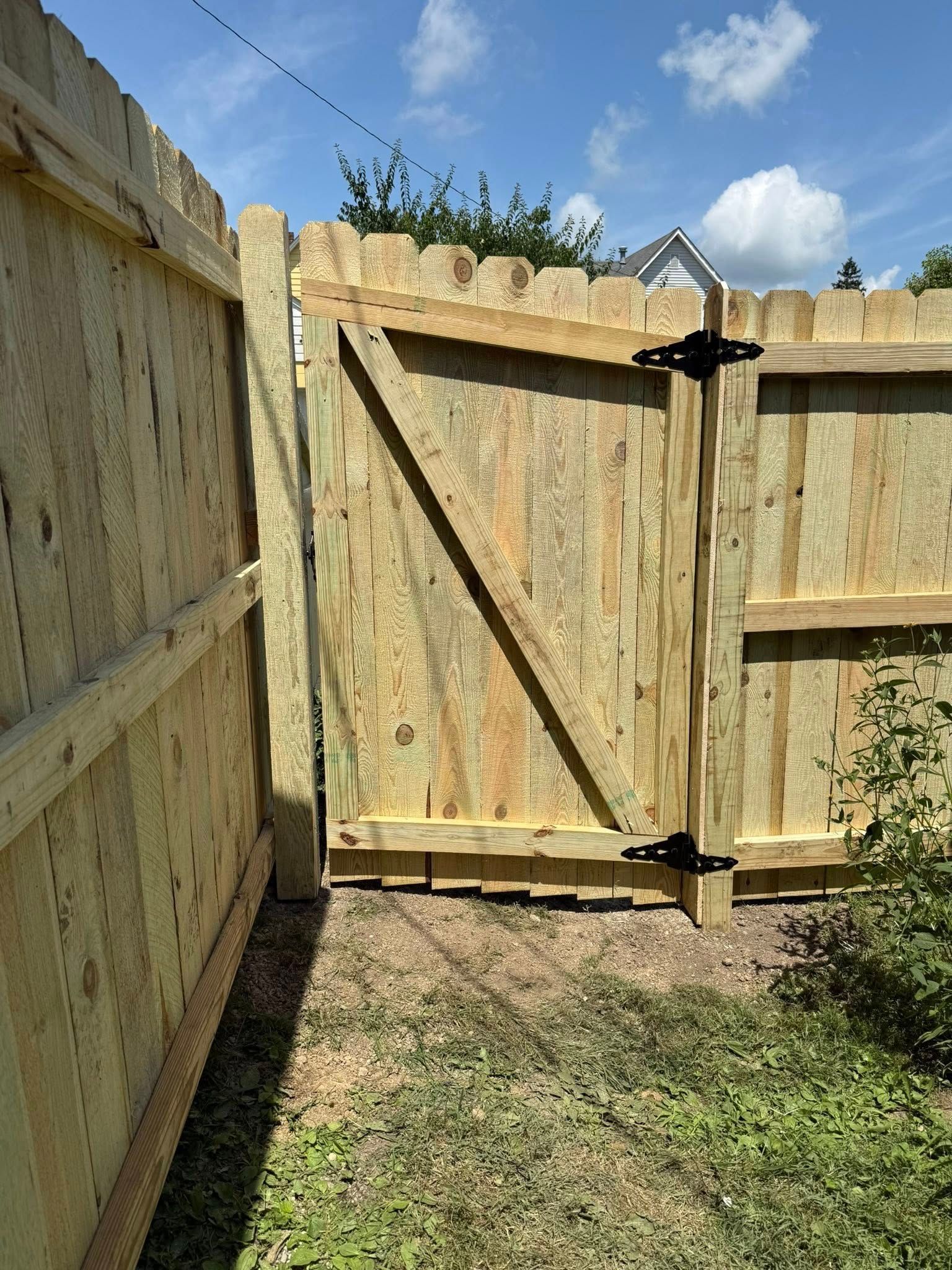 Wooden fence with a gate in an outdoor setting, angled brace, blue sky.
