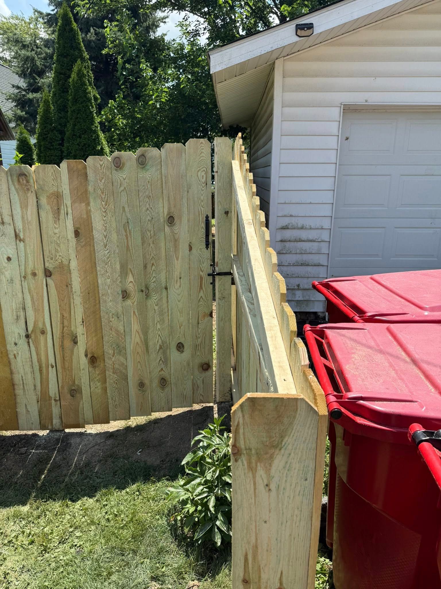Wooden fence next to a white garage. Two red trash bins are on the right.