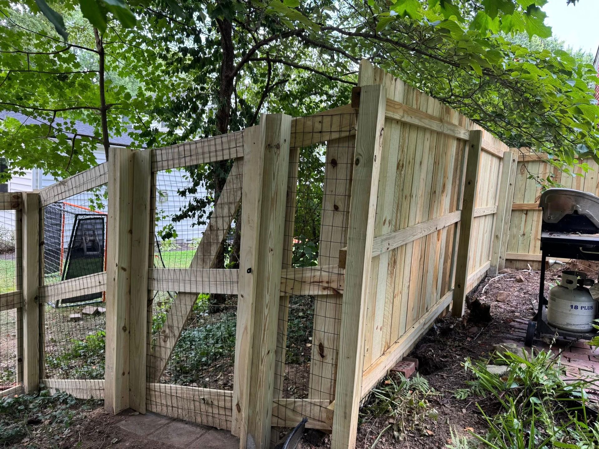 New wooden fence in a backyard with a grill and trees.